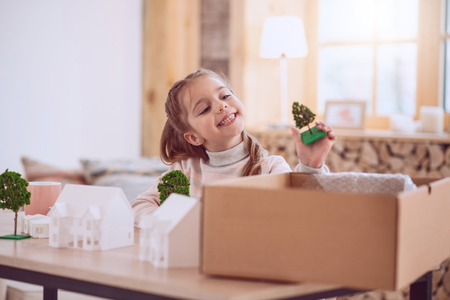 Interesting game. Happy cute girl holding a tree model while playing at homeの写真素材