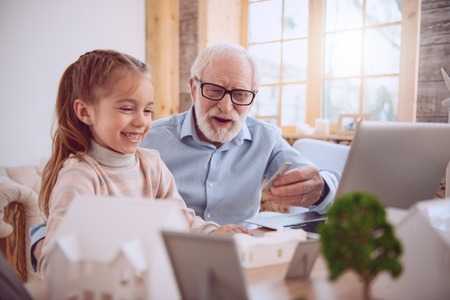 Positive aged man sitting near his pupil while giving her a lesson
