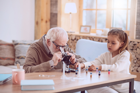 Professional scientist. Serious elderly man sitting together with his granddaughter while workingの写真素材