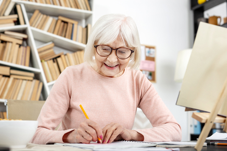 Jovial senior woman studying while using pencilの写真素材