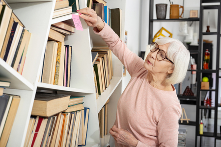 Organized mature woman placing sticker hieroglyph shelf and staring upの写真素材