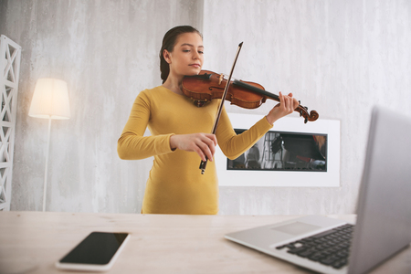 Attentive young female using her instrument while learning classical workの写真素材
