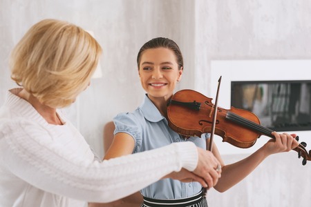 Joyful young woman keeping smile on her face while playing the violinの写真素材