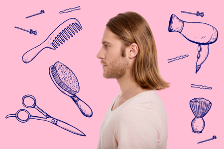 Profile of young handsome light haired man preparing for a date while standing against pink backgroundの写真素材