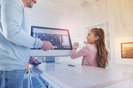 So funny. Cheerful emotional pupil standing with a modern tablet and laughing while looking at her positive tutorの写真素材