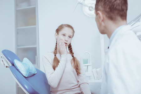Teeth pain. Beautiful sad girl touching face while looking at male dentistの写真素材