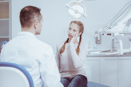 Teeth problem. Gloomy attentive girl touching cheek while looking at male dentistの写真素材