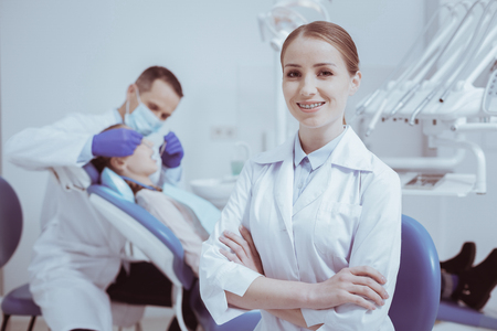 Ready for work. Inspired glad female dental assistant crossing arms and smiling to cameraの写真素材