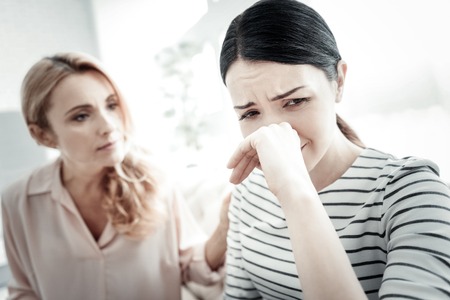 Im stuck. Disappointed unhappy tired woman sitting o the sofa touching her nose and crying.の写真素材