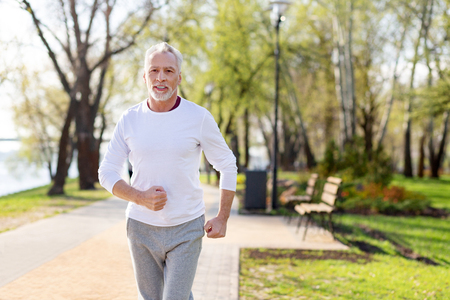 Healthy lifestyle. Joyful aged man jogging while caring about his healthの写真素材