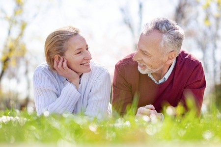 Aged couple. Happy nice people looking at each other while lying in the grassの写真素材