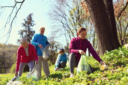 Helping nature. Beautiful happy woman gathering litter while other volunteers helping her