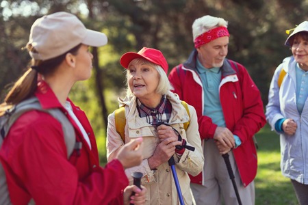 Having a walk. Cheerful blond woman smiling and talking with the guide while hikingの写真素材