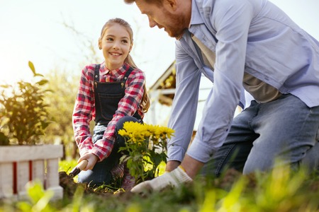 With family. Positive happy girl smiling while working together with her father in the gardenの写真素材