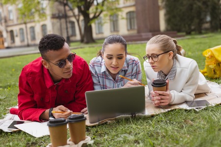 Three smart students feeling involved in preparing for complicated language test in the park togetherの写真素材