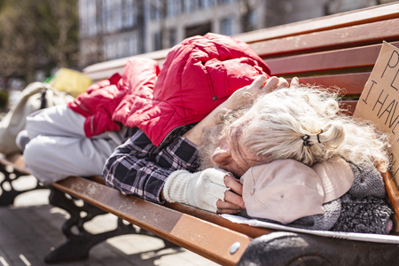 Housing crisis. Aged homeless man resting on the street while not having a place to itの写真素材