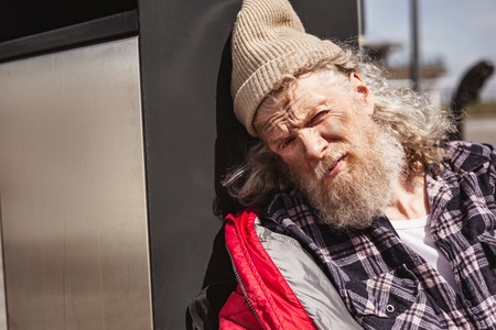 Social problem. Depressed poor man looking at you while leaning on to the litter binの写真素材