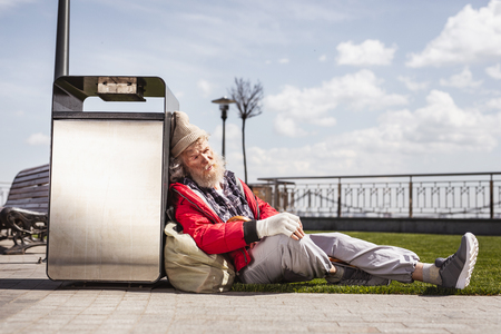 I am tired. Cheerless port man leaning on to the litter bin while restingの写真素材