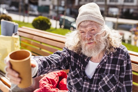 Life challenge. Poor bearded man holding a plastic cup while being in the need for moneyの写真素材