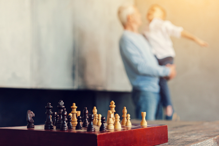 Emotional moment. Happy cheerful grandfather holding a delighted grandson in his arm after playing chess togetherの写真素材