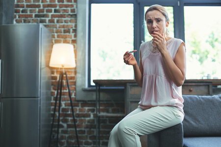 Infertility for woman. Low angle of troubled mature woman staring at camera and holding pregnancy testの写真素材
