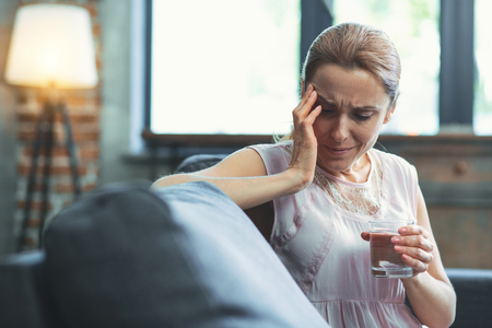 Pessimistic thoughts. Unhappy mature woman carrying glass of water and cryingの写真素材