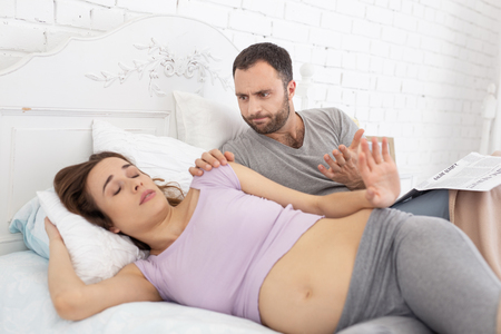 Angry man waking up pregnant woman who sleepingの写真素材