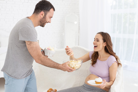 Cheerful pregnant woman choosing food while man standingの写真素材