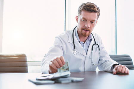 Breaking the law. Male professional doctor sitting at the table and taking bribesの写真素材