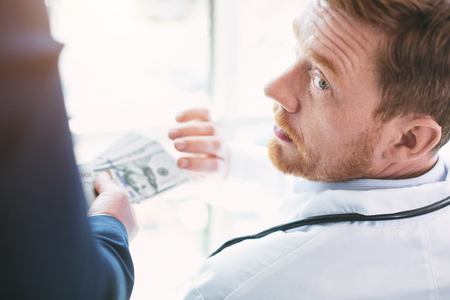 Money decided everything. Amoral unprincipled doctor wearing a uniform and a man giving him a bribeの写真素材