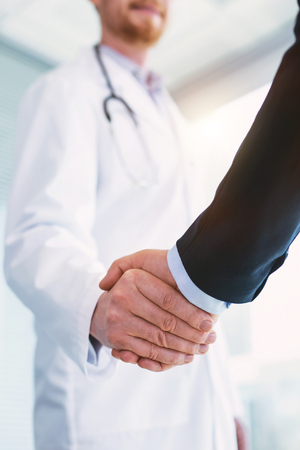 Inspired professional doctor wearing a uniform and shaking hands with a businessmanの写真素材