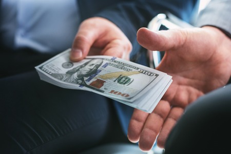 Influential wicked businessman sitting next to another businessman and giving him a bribeの写真素材