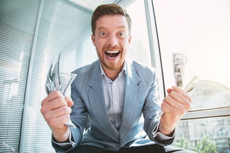 Pleased greedy man smiling and holding a lot of moneyの写真素材