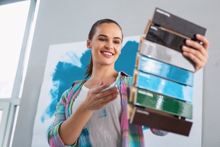 Joyful young woman smiling and picking a colour of paintの写真素材