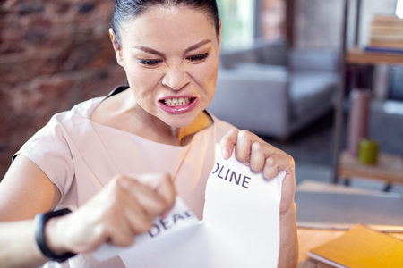 Stress management. Wrathful female employee tearing paper and posing on blurred backgroundの写真素材