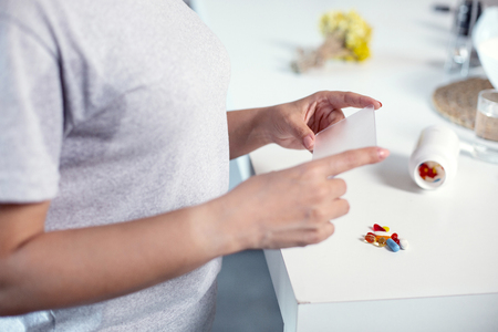 Useful medication. Close up of attractive female hands holding plastic and pills lying on tableの写真素材