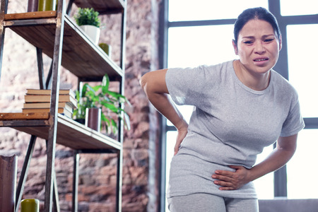 Common cold. Low angle of sincere painful woman standing and touching belly