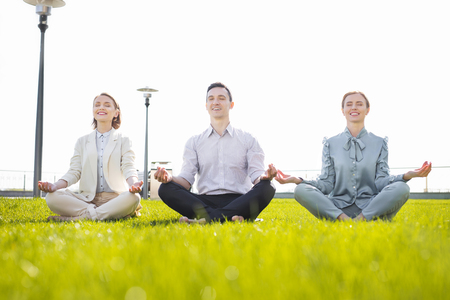 Yoga practice. Three stressed office workers feeling relaxed while practicing yoga outside the officeの写真素材