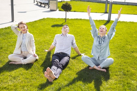 Break time. Three chief executives feeling amazing spending their break time outside the office sitting on the grassの写真素材