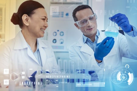 Happy chemists. Cheerful emotional chemists sitting together in a lab and smiling while looking at the blue liquid in a bottleの写真素材