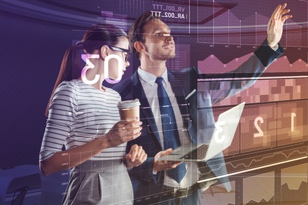 Friendly atmosphere. Clever programmer standing with a laptop in his hands and his friendly coworker holding tasty coffeeの写真素材