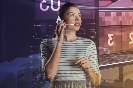 Phone conversation. Clever professional database administrator thoughtfully looking at the information on the screen while talking on the phoneの写真素材