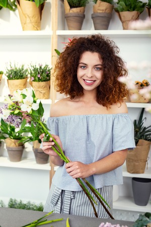 Flower decorator. Delighted nice woman holding flowers while working in the flower shopの写真素材