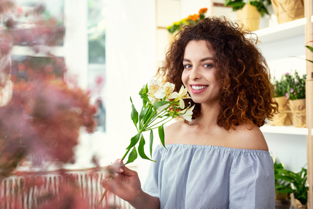 Positive mood. Happy attractive woman smiling while holding flowersの写真素材