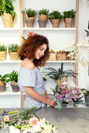 Creativity in work. Nice skillful florist looking at the flower bouquet while enjoying her workの写真素材