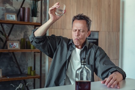 Awful day. Grey-haired mature alcoholic feeling in despair while finishing his glass of whisky after awful dayの写真素材