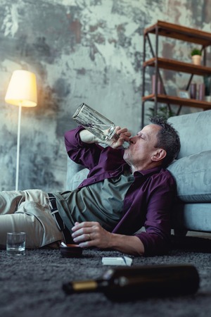 Drinking vodka. Real alcoholic drinking cheap vodka from the bottle while lying on the floor at his...