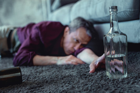 Pushing hand. Mature grey-haired drunk man looking disgusting while pushing his hand after bottle of vodkaの写真素材
