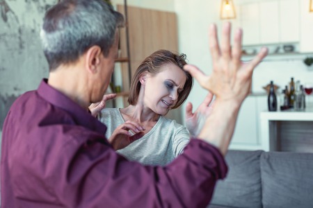 Lifting hand. Grey-haired elderly man feeling furious and angry while lifting his hand against crying wifeの写真素材