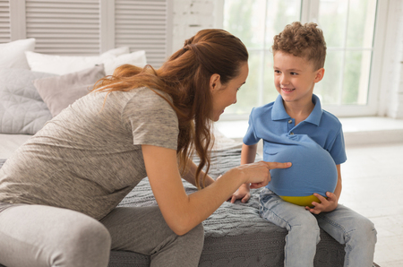 Entertaining son. Appealing dark-haired pregnant expecting woman feeling extremely happy while entertaining her little sonの写真素材